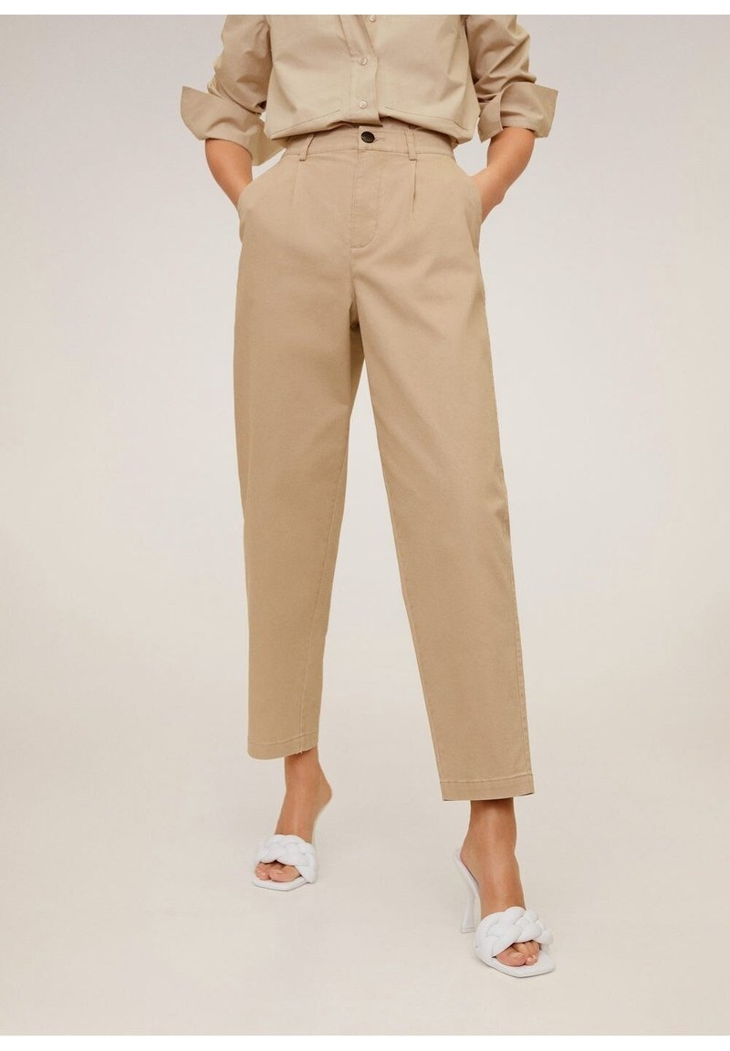 Pantalons en coton beige à coupe ajustée, dotés de poches avant et d'une fermeture à un bouton, associés à des sandales blanches tressées.
