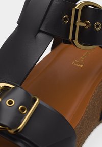 Μαύρο δερμάτινο σανδάλι πλατφόρμα με αγκράφες σε χρυσό τόνο και πάτο από φελλό, με λείο καφέ πέλμα.