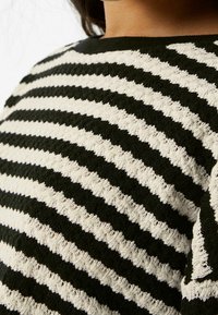 Pull en maille rayé présentant des couleurs alternées noir et crème, avec un motif texturé. Encolure ronde et tissu doux.