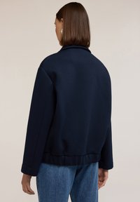 Felpa blu navy con vestibilità rilassata, ampio colletto e orlo a costine. Presenta una texture liscia e spalle scese per un look comodo.