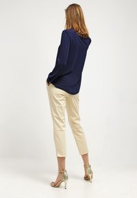 Námornická blouse s dlouhým rukávem v kombinaci s béžovými společenskými kalhotami a metalickými sandály na vysokém podpatku. Hladká tkanina, dobře padnoucí střih a délka ke kotníkům.