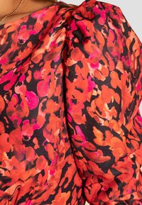 Top floreale con un vivace motivo di tonalità rosse e rosa su uno sfondo nero, realizzato in tessuto morbido e fluente, con maniche gather.