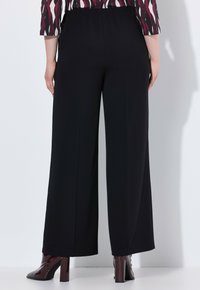 Zwarte wijde broek gemaakt van een gladde stof, met een elastische tailleband. Gecombineerd met glanzende burdeos haklaarzen.