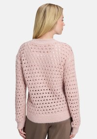 Jasnoróżowy sweter z dzianiny o otwartym fasonie, długie rękawy i ściągacz u dołu. Miękka faktura, luźny krój i casualowy styl.