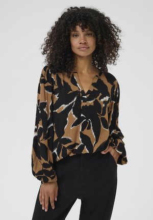Blouse ample avec un mélange de motifs noirs, bruns et blancs ; décolleté en V, manches longues, tissu texturé. Porte avec un pantalon noir.