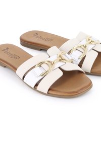 Sandalias deslizantes blancas y beige con suela plana, que presentan un detalle de hebilla dorada brillante y una textura suave en las correas.