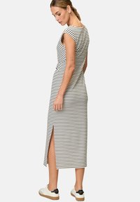 Striped midi dress in black and white, featuring cap sleeves, side slit, and a fitted silhouette. Worn with white sneakers and a natural texture.