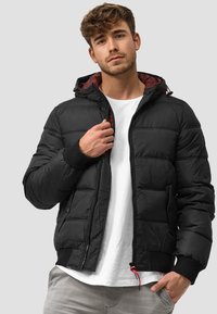 Schwarze gepolsterte Jacke mit Kapuze, ausgestattet mit einem Reißverschluss vorne, elastischen Bündchen und einem kontrastierenden roten Innenfutter. Glatte Textur und lässiger Schnitt.