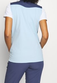 Light blue athletic top with a navy collar, short sleeves, and a smooth texture, paired with dark blue athletic pants.