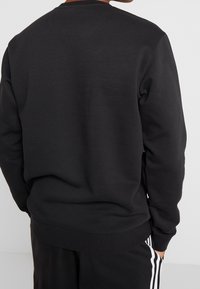 Sweat-shirt noir avec un col rond, des manches longues et une texture douce. Aucun logo ou motif visible; design décontracté.
