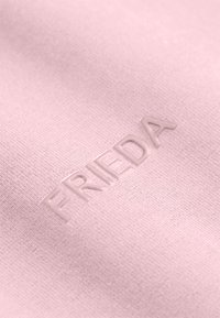 Lichtroze stof met een gestructureerd oppervlak, met een gegraveerd "FRIEDA" logo in een subtiel, verheven ontwerp.