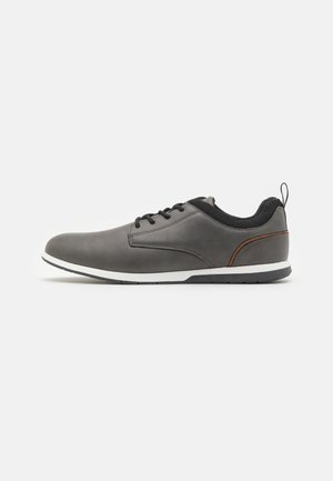 Chaussures en cuir gris avec accents noirs, présentant un bout arrondi, un design à lacets, une semelle blanche et une petite languette à l'arrière.