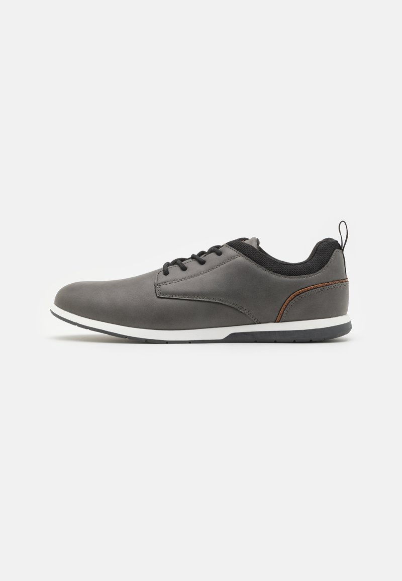Chaussures en cuir gris avec accents noirs, présentant un bout arrondi, un design à lacets, une semelle blanche et une petite languette à l'arrière.