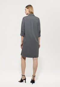 Graues Kleid mit Kragen, dreiviertelärmel, Rückenschlitzdetail und Seitenschlitzen, kombiniert mit schwarzen High-Heel-Sandalen.