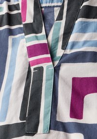 Camisa de algodón con un patrón geométrico multicolor en azul marino, púrpura, verde azulado y blanco, con un diseño de cuello en V y costuras en contraste.
