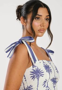Vestido blanco con estampado de palmeras moradas, que presenta tirantes anchos a rayas para ajuste y un panel fruncido en el costado para un mejor ajuste.