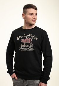 Felpa nera con stampa grafica di un maiale e testo che recita "PorkyPete's Brooklyn Prime Cuts" sul davanti. Collo rotondo e maniche lunghe.