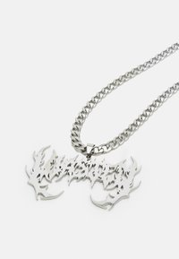 Silver chain necklace with a large, intricate pendant featuring sharp, flame-like details and an engraved text design.