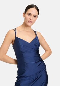 Satin ärmlös klänning i djup marinblå, med V-hals och samlad sidodetalj som skapar en slät, draperad silhuett.
