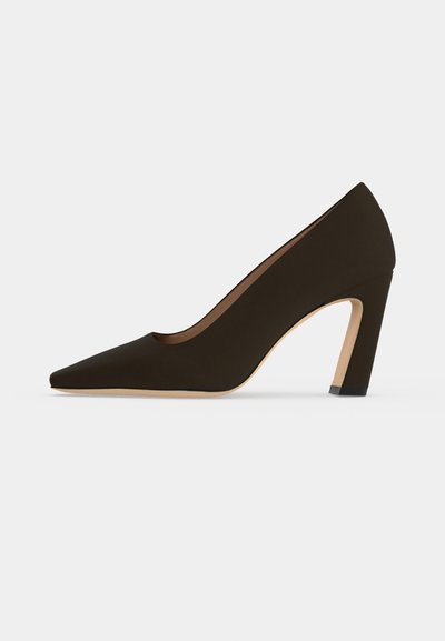 Escarpin marron foncé à bout pointu et à talon haut, avec une semelle beige, présenté de profil sur un fond uni.