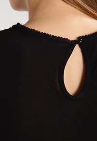 T-shirt noir avec un col rond, présentant une découpe en forme de clé à l'arrière et une délicate bordure festonnée le long du col.