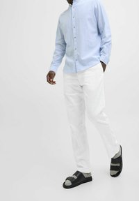 Světle modrá košile na knoflíky, bílé kalhoty a černé sandály se šedými detaily. Oblečení má volný střih a jednoduchý design.