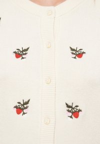 Καφέ ζακέτα με ραβδωτή υφή, στολισμένη με ροζ και κόκκινες κεντημένες φράουλες και πράσινα φύλλα, κλειστή με κίτρινα κουμπιά.