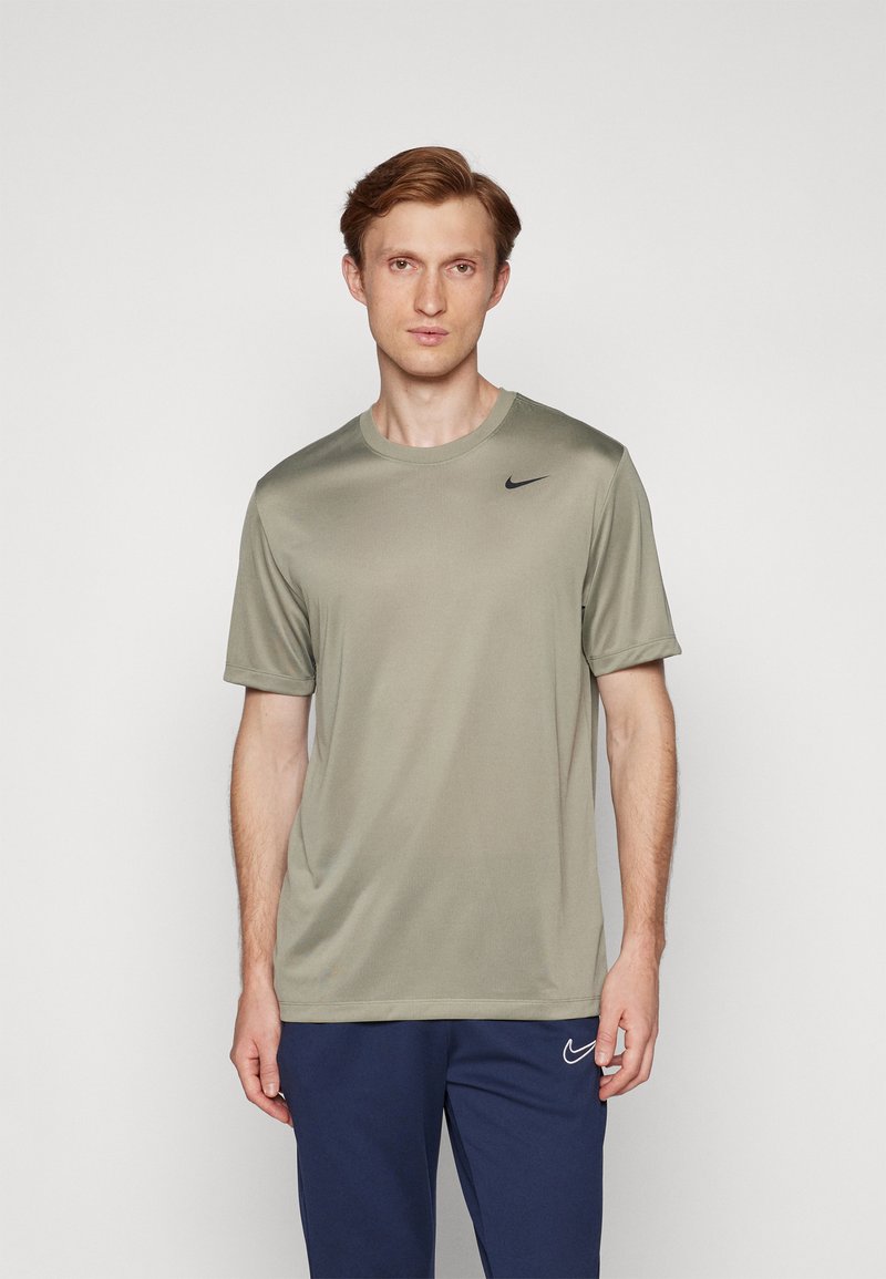 Tricou Nike de culoare verde măsliniu, cu guler rotund, mâneci scurte și un logo negru pe pieptul stâng. Țesătura pare netedă și ușoară.
