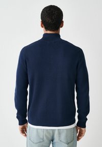 Marineblauer Strickpullover mit hohem Kragen und gerippten Bündchen. Verfügt über eine glatte Textur und einen taillierten Schnitt, sichtbare Nähte und einen schlichten Stil.