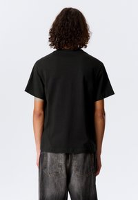 Černé tričko s volným střihem, krátkými rukávy a kulatým výstřihem. Vyrobené z bavlněné tkaniny s hladkou texturou.