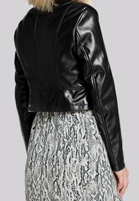 Chaqueta corta de piel sintética negra con mangas largas, costuras detalladas y una textura suave, combinada con una falda de estampado de serpiente.