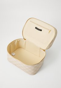 Beige kosmetikväska med präglat mönster, dragkedjestängning och en slät insida. Innehåller ett fack med dragkedja och en tyglabel på insidan.