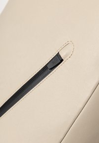 Borsa in pelle beige con zip nera e un tirante. La superficie è liscia con una leggera lucentezza e un design pulito e minimalista.