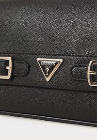 Black textured handbag with gold-tone hardware, featuring a triangular brand logo and buckle accents on a smooth strap.
