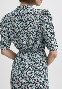Rochie florală cu un fundal negru, flori roz și albastre, mâneci bufante, guler înalt și talie strânsă pentru o siluetă structurat.