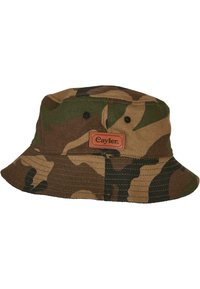 Chapeau seau Cayler en camouflage dans un tissu marron et vert, avec une visière plate, un couronne décontractée et un patch en cuir avec le logo à l'avant.