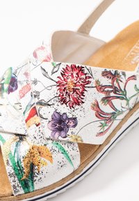 Vita blommönstrad sandal med korsade remmar, vadderat innersulor, strukturerad yta och en subtil glittrig finish. Gummisula med en lätt platå.