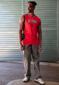 Piros ujjatlan póló "CHICAGO" felirattal és logóval, szürke bővérű farmernadrág, fekete napszemüveg, fehér és fekete sportcipő, kis fekete keresztpántos táska.