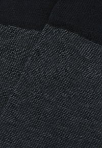 Tejido de punto oscuro con una superficie texturizada, que presenta un patrón combinado de colores gris oscuro y negro, mostrando un acabado suave.