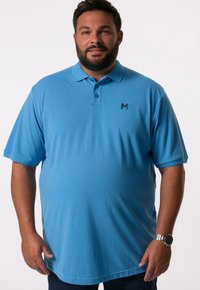 Světle modré polo tričko vyrobené z bavlny, s límečkem, dvěma knoflíky, krátkými rukávy a malým černým logem na hrudi.