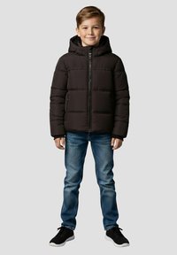 Sort puffervest med hætte, quiltet design, lynlås foran og to sidelommer, båret over blå jeans og sorte sneakers.