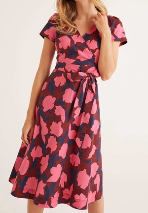 Woman wearing a short-sleeve, V-neck wrap dress with large pink and navy floral patterns on a brown background.