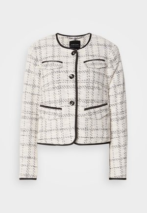 Veste pour femme en tweed blanc et noir avec col rond, quatre boutons noirs, poches à rabat décoratives, ourlée de passepoils noirs.