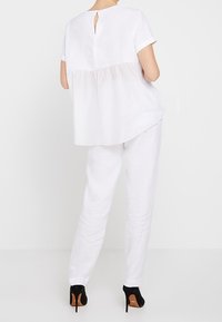 Haut en lin blanc, ample, à manches courtes et avec un détail en forme de trou de serrure au dos, associé à un pantalon en lin blanc et des chaussures à talons hauts noires.