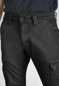 Pantalones cargo negros de mezclilla, con una superficie texturizada, múltiples bolsillos y un cierre de botón en la cintura.