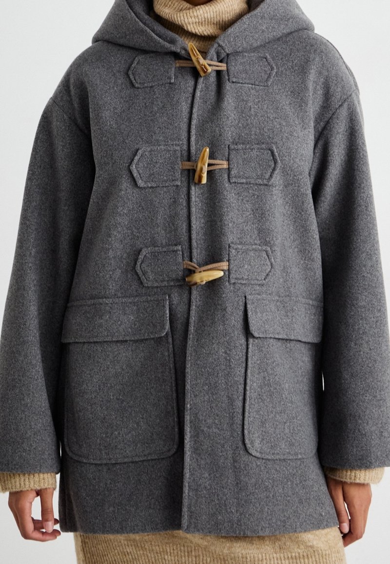 Grå duffelcoat lavet af uld med hætte, der har træknap-lukninger, to forlommer og ribbede ærmegab. Enkel, struktureret stof.