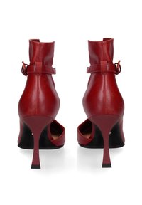 Scarpe rosse in pelle con tacco alto e cinturini alla caviglia, caratterizzate da una punta affilata e un sottile tacco a stiletto. Texture liscia e design minimalista.