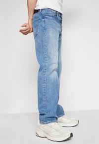 Lichtblauwe denim jeans met een rechtvallende pasvorm, voorzien van subtiele stikseldetails, voor- en achterzakken, gecombineerd met lichtgekleurde sneakers.