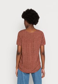 Top de flores castanho de mangas curtas com decote redondo e detalhes franzidos nas costas, combinado com jeans largos azuis. Tecido de textura suave.