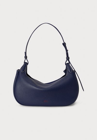 Temno modra usnjena torbica s ukrivljenim silhueto, teksturirano površino in tankim nastavljivim trakom; na njej je diskretna rdeča znamka.